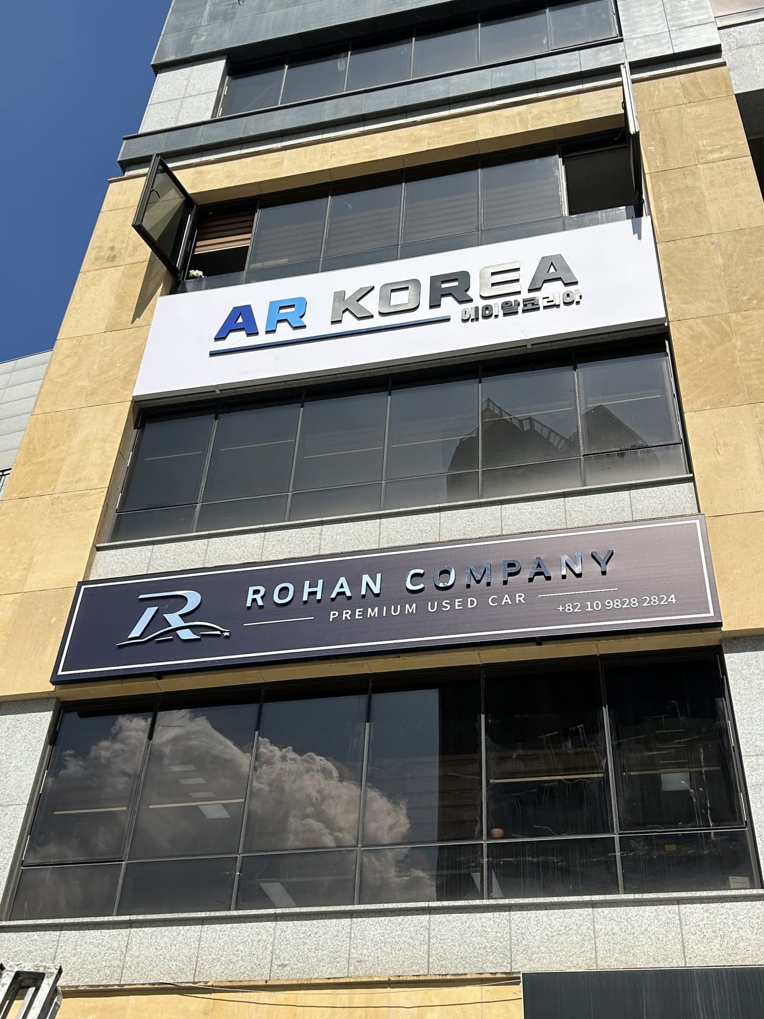 The Rohan Company signboard mounted on the front of the building: the silver R mark beside “ROHAN COMPANY”, and under it “PREMIUM USED CAR”. A second tenant’s sign, AR KOREA, sits on the floor above.